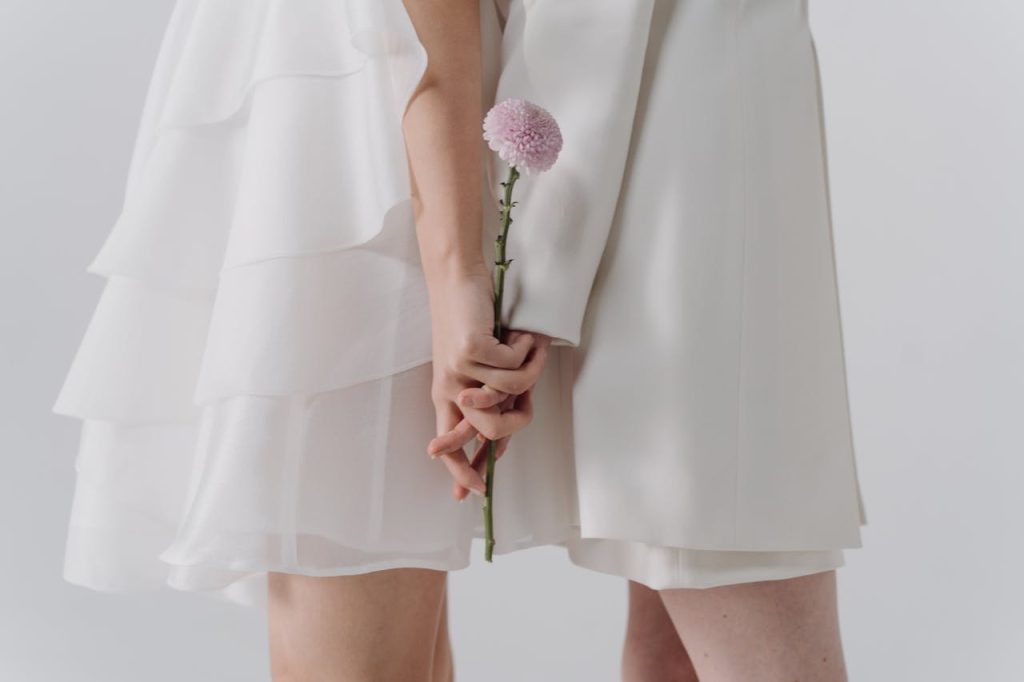 A romantic scene with a couple in white holding a single pink flower, symbolizing love and elegance.