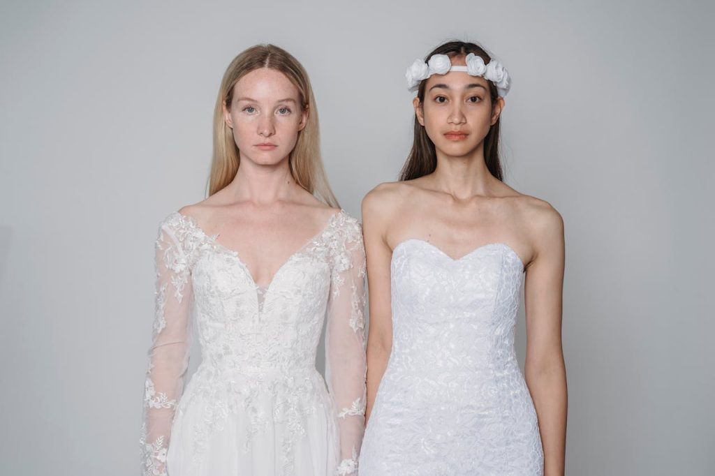 Two women in delicate white bridal gowns showcasing wedding fashion.